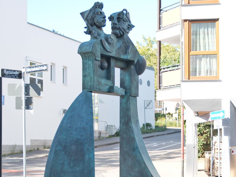 Jürgen Goertz, Ungleiches Paar, 1995 (Detail). Ausschnittaufnahme des Ungleichen Paares von Jürgen Goertz. Ein Frauenkopf und ein Männerkopf vor dem Hintergrund der Bahnhofsanlage.